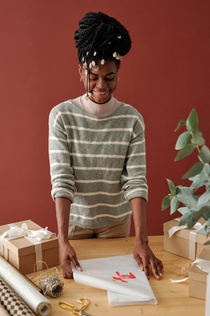 Happy African American girl wrapping Christmas gift into wrap paper with handmade red deer print...
