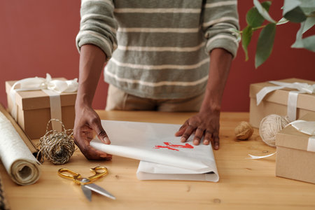 Hands of unrecognizable African American girl preparing xmas presents and wrapping them into white paper with red deer printの写真素材