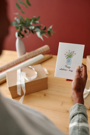 Handmade greeting card with drawing of vase with flowers held by young unrecognizable African American woman preparing for holidayの写真素材
