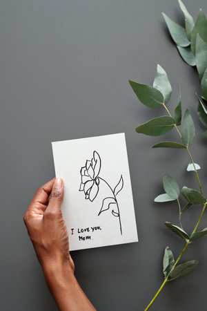 Hand of unrecognizable African American woman holding handmade greeting postcard with wishes and love for Mother Dayの写真素材