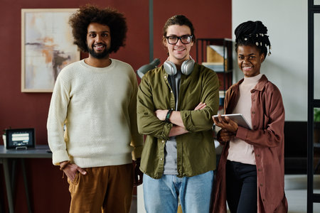 Three happy young intercultural office workers in casualwear standing in front of camera and looking at you in coworking spaceの写真素材