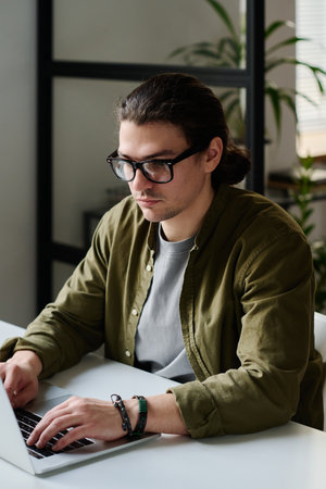 Serious male AI designer in casualwear looking at laptop screen and typing on laptop keyboard while working over new design projectの写真素材