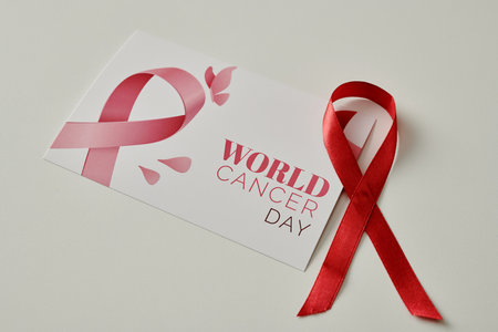 Pink ribbon in shape of loop lying on white desk next to handmade postcard prepared for world cancer day and prevention campaignの写真素材