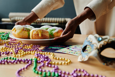 Young unrecognizable African American woman putting plate with appetizing homemade pastry on table with beads and maskの写真素材