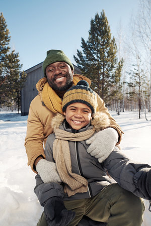 Happy young African American man and his cute son in warm winterwear taking selfie and looking at camera on winter weekendの写真素材
