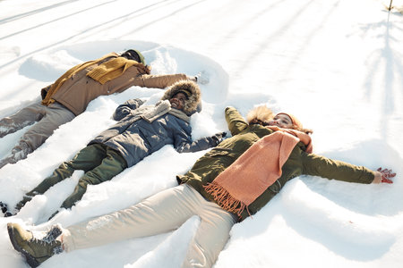 Three cheerful intercultural people in winterwear lying in snowdrift while playing and having fun at leisure or during winter vacationの写真素材