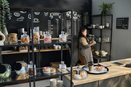 Display with appetizing sweets and desserts standing in front of camera next to wooden counter with order of client on tray and clocheの写真素材