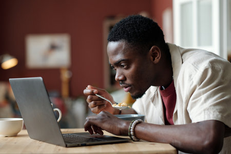 Young man looking at laptop screen while watching online video or communicating with someone in chat...