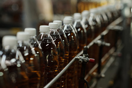 Row of packed plastic bottles containing soda with white caps moving along assembly line or belt conveyor in large factoryの写真素材