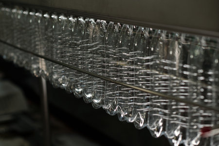 Empty and clean plastic bottles moving along production line inside huge industrial machine inside...
