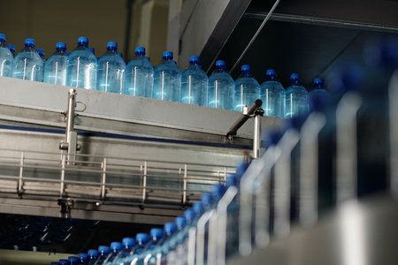 Row of capped plastic bottles with still and carbonated mineral water moving on huge assembly line...