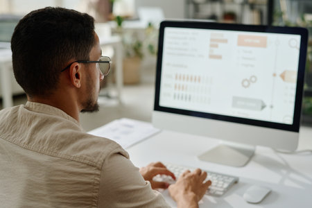 Young ceo or entrepreneur looking at computer screen and analyzing data or organizing work while...