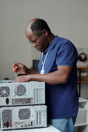 Professional male technician fixing details of computer hardware with screwdriver while standing by workplace in front of cameraの写真素材