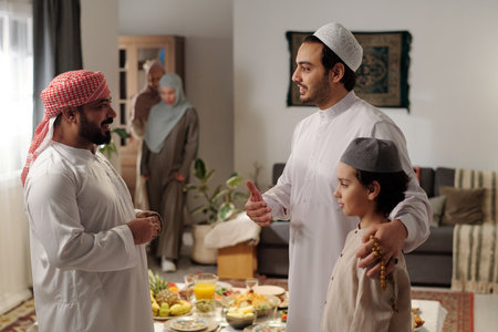 Mature Middle Eastern man talking to his younger brother and nephew at family gathering on Eid...