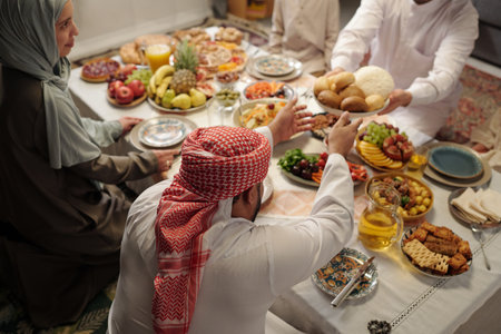 High angle view of young Muslim man sharing food with his family at festive dinner on Uraza Bayram