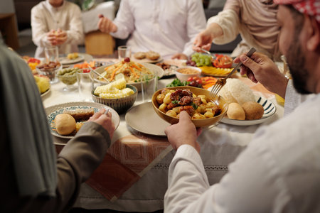 Selective focus over-shoulder shot of unrecognizable Muslim family sitting at festive table having dinner on Eid Al-Fitrの写真素材