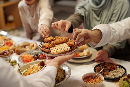 Selective focus shot of hands of Muslim people taking sweet biscuits from plate unrecognizable man holding during family dinnerの写真素材