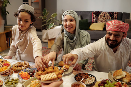 Happy Muslim man, woman and kid taking desserts from plate unrecognizable man holding at family dinner on Uraza Bayramの写真素材