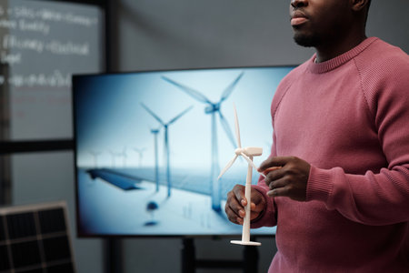 Cropped shot of young male manager with model of windmill in hands standing against interactive board with visual template of his projectの写真素材