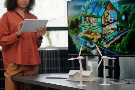 White plastic windmills standing on desk against house model and screen with visual template of new business project during presentationの写真素材