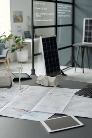 Digital tablets, mockups of windmill and houses, unrolled blueprint with sketch of new construction...