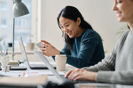 Two young Asian and Caucasian women wearing smart casual clothes enjoying conversation at work in modern office, selective focusの写真素材