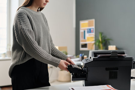 Crop shot of young Caucasian female office worker wearing gray sweater changing ink cartridge in printer, copy spaceの写真素材