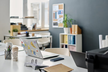 No people shot of part of modern office interior with laptop, smartphone and documents on table,...