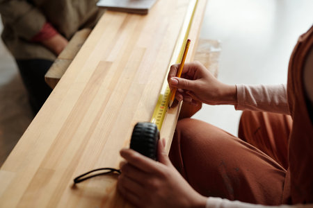 Hand of young unrecognizable African American female designer with pencil and measuring tape taking measures of wooden boardの写真素材