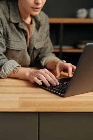 Hands of young female designer or solopreneur typing on laptop keyboard by counter while organizing work in cafe after refitの写真素材