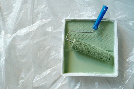 Top view of plastic tray with paintroller and green paint standing on the floor covered with cellophane and prepared for renovation workの写真素材