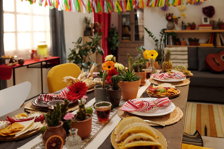 Part of long wooden table decorated by gerberas and domestic cactuses in flowerpots and served with various homemade snacks for dinnerの写真素材