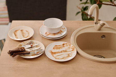 Several dirty plates, knives, porcelain bowl, steel spoon and fork ready to be washed standing on...