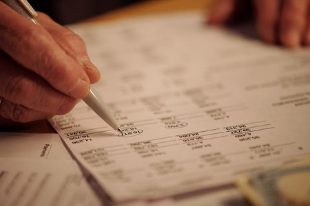 Close-up of hand of elderly woman with pen circling sum on unpaid financial paper document while...