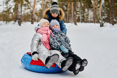 Group of three adorable children in winterwear laughing and looking at camera while having fun in...