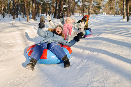 Group of joyful kids in winterwear screaming while moving down hill on snow tubes and slides and...