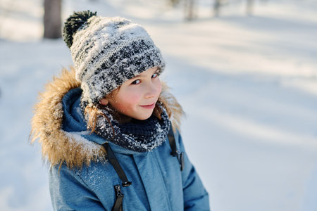 Cute smiling boy in grey knitted beanie hat and blue winter jacket looking at camera while walking...
