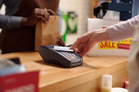 Hand of young unrecognizable female customer holding credit card over terminal during contactless payment for skincare productsの写真素材