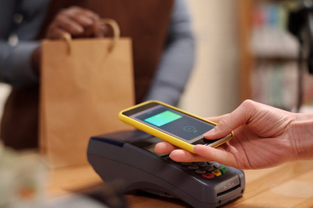 Hand of young female shopper with smartphone making contactless transaction while holding gadget...