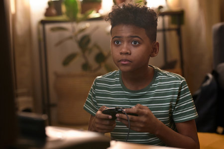 African American teenage boy with short curly hair playing retro video game, focused on the screen...
