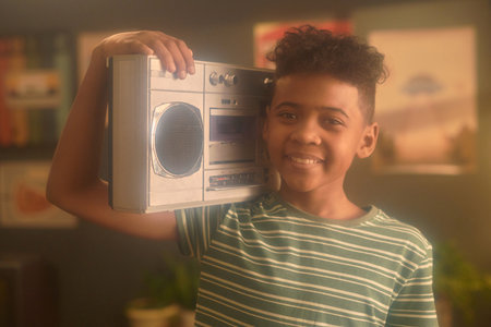 Portrait of African American boy smiling and holding boombox on shoulder, showcasing retro vibe in...