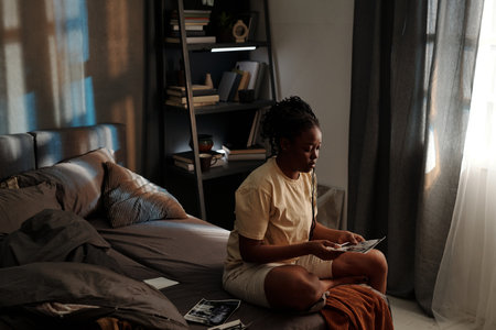 Young depressed woman looking through photographs of her ex husband or boyfriend or dead member of her family while sitting on bedの写真素材