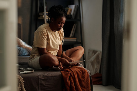 Young unhappy African American woman with picture of her died husband or boyfriend sitting on bed at home in the middle of the nightの写真素材
