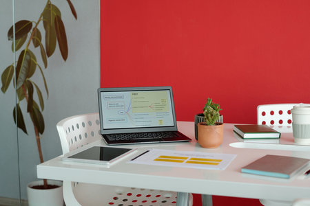 Office desk with laptop, stationery, digital tablet, coffee cup and plant in modern workspace with red wallの写真素材