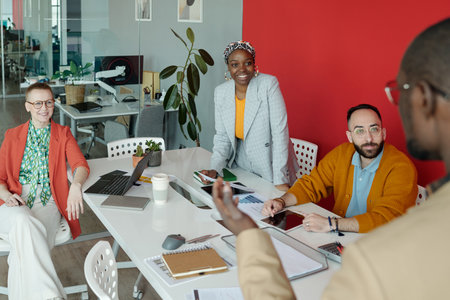 Multi-ethnic team of colleagues collaborating during office meeting, with laptops and documents on...