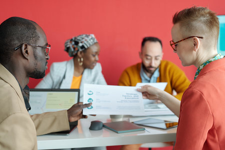 Multi-ethnic team of colleagues analyzing documents and discussing strategy during office meeting in...