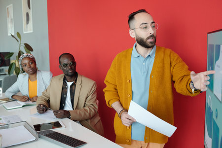 Caucasian businessman presenting ideas on large screen to African American colleagues listening attentively during office meetingの写真素材