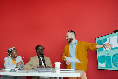 Man conducting engaging presentation with team in modern office setting with red wall and large...
