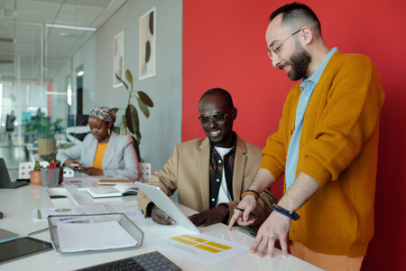 Professionals collaborating on digital project in contemporary office setting. Two men discussing...