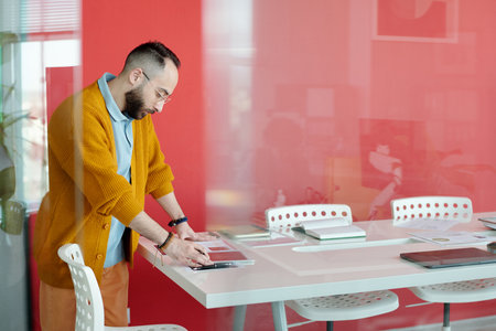 Caucasian man in business casual attire using digital tablet at office desk. He is focused on his...